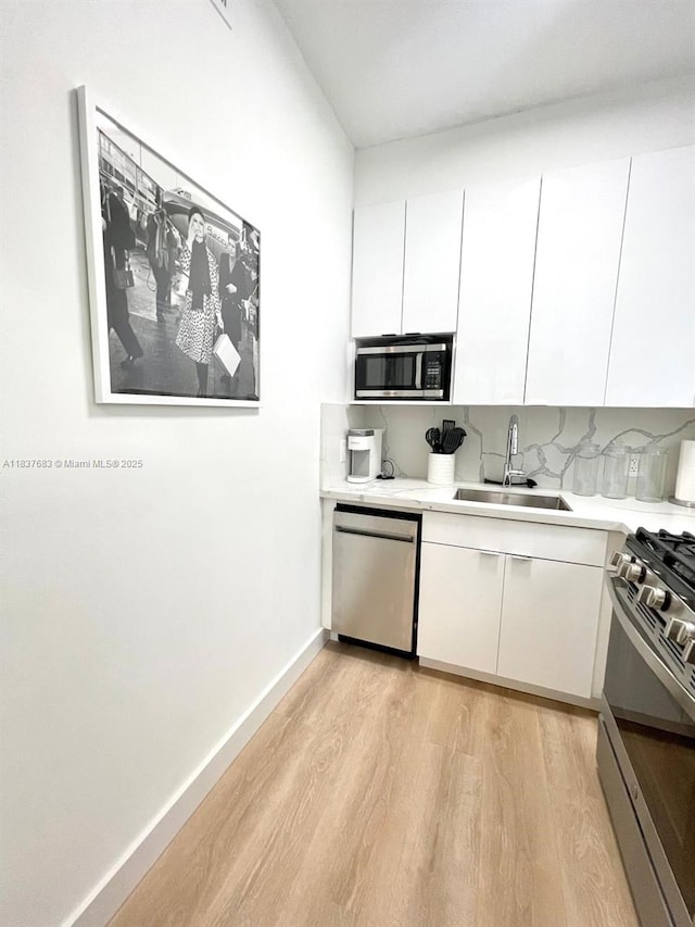 936 Pennsylvania Ave Unit 101, Miami Beach, FL 33139 - kitchen featuring appliances with stainless steel finishes, light wood-type flooring, light countertops, and white cabinets