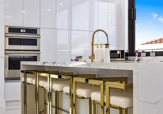 2225 NE 19th St, Fort Lauderdale, FL 33305 - kitchen featuring stainless steel double oven, modern cabinets, white cabinets, and a breakfast bar