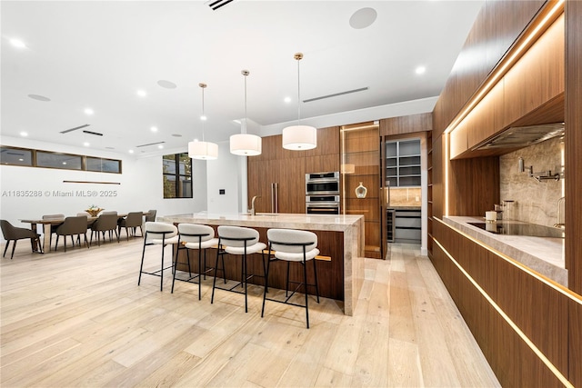 260 NW 47th St, Miami, FL 33127 - kitchen with modern cabinets, brown cabinetry, a kitchen breakfast bar, light wood-type flooring, and a spacious island