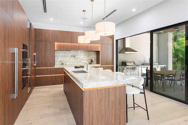 260 NW 47th St, Miami, FL 33127 - kitchen with modern cabinets, brown cabinetry, decorative backsplash, a kitchen bar, and a center island with sink