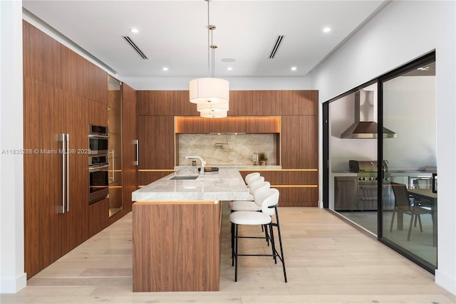 260 NW 47th St, Miami, FL 33127 - kitchen with wall chimney exhaust hood, modern cabinets, brown cabinets, light wood-style floors, and recessed lighting