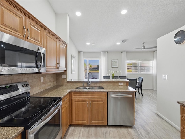 4024 Summer Chase Ct, Lake Worth, FL 33467 - kitchen with appliances with stainless steel finishes, light wood finished floors, a peninsula, brown cabinets, and decorative backsplash