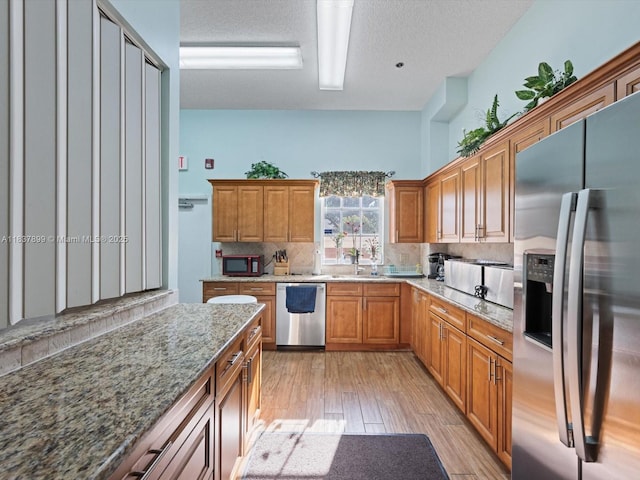 4024 Summer Chase Ct, Lake Worth, FL 33467 - kitchen featuring appliances with stainless steel finishes, backsplash, light wood-type flooring, light stone counters, and brown cabinetry