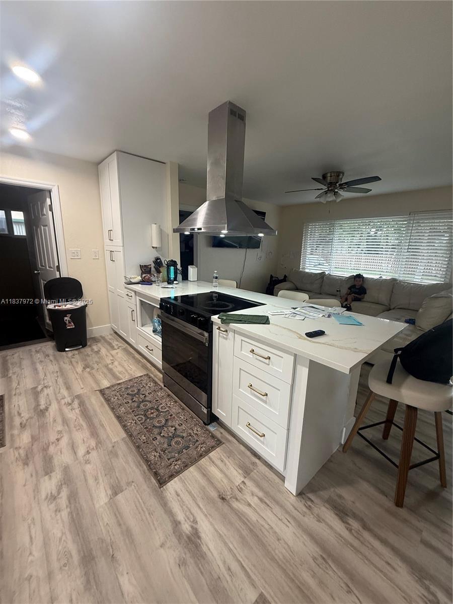 2485 NW 84th Way, Sunrise, FL 33322 - kitchen with island exhaust hood, electric range oven, light wood finished floors, white cabinets, and ceiling fan