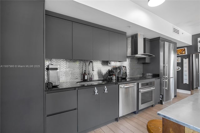 720 NE 62nd St Unit 301, Miami, FL 33138 - kitchen featuring wall chimney range hood, appliances with stainless steel finishes, dark countertops, gray cabinets, and light wood-type flooring