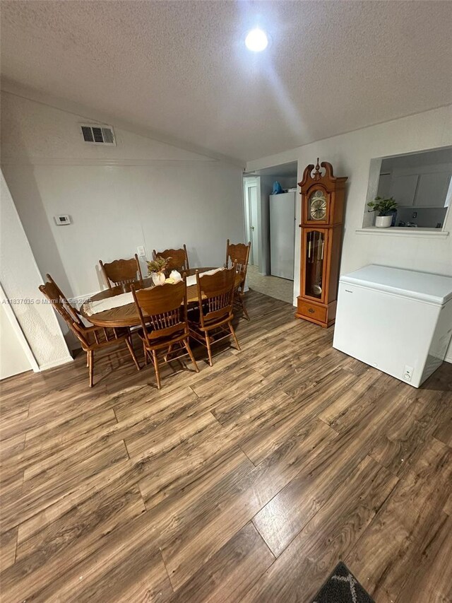 dining area with wood finished floors, a textured ceiling, and vaulted ceiling