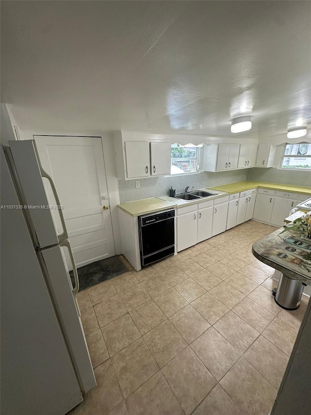 kitchen featuring freestanding refrigerator, black dishwasher, white cabinets, light tile patterned floors, and light countertops