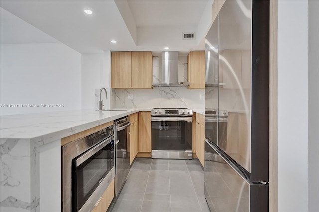 5600 Collins Ave Unit 10L, Miami Beach, FL 33140 - kitchen featuring wall chimney range hood, appliances with stainless steel finishes, light brown cabinets, a peninsula, and recessed lighting