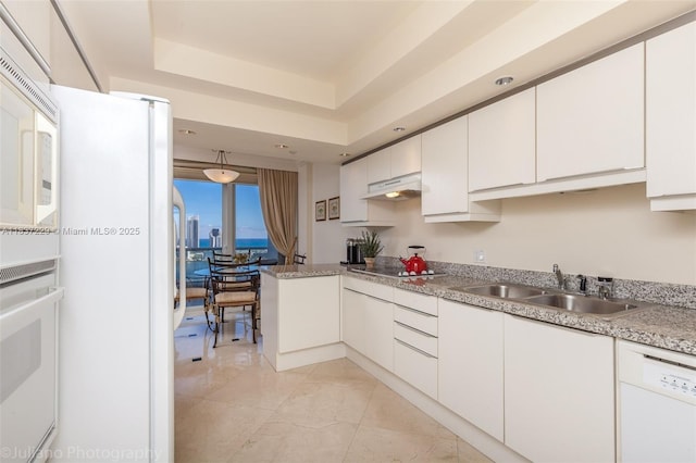 7000 Island Blvd Unit 2504, Aventura, FL 33160 - kitchen featuring under cabinet range hood, white appliances, white cabinets, a peninsula, and a raised ceiling