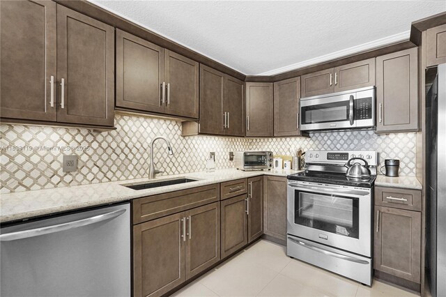 12650 SW 6th St Unit 101K, Pembroke Pines, FL 33027 - kitchen featuring stainless steel appliances, dark brown cabinetry, light stone countertops, tasteful backsplash, and a textured ceiling
