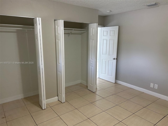4021 NW 7th Ave, Deerfield Beach, FL 33064 - unfurnished bedroom with a textured ceiling, light tile patterned flooring, and two closets