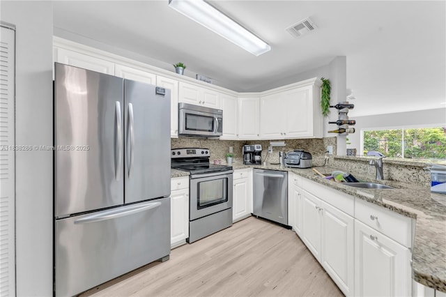 10104 Royal Palm Blvd Unit 107-C, Coral Springs, FL 33065 - kitchen with appliances with stainless steel finishes, light wood-style floors, white cabinetry, decorative backsplash, and light stone countertops