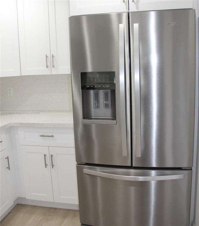 1075 W 68th St Unit 110, Hialeah, FL 33014 - detailed view of stainless steel refrigerator with ice dispenser, white cabinets, light wood-style flooring, and light stone counters