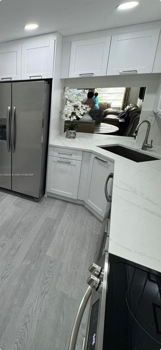7480 NW 17th St Unit 103, Plantation, FL 33313 - kitchen featuring stainless steel refrigerator with ice dispenser, white cabinetry, light wood finished floors, and light stone counters