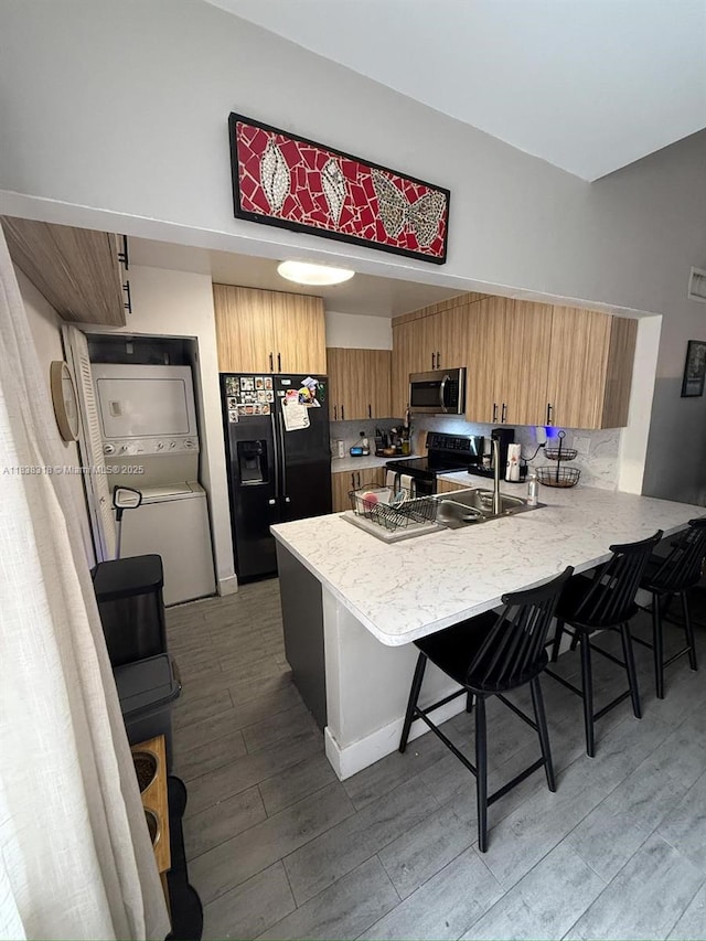 575 W Park Dr Unit 202, Miami, FL 33172 - kitchen featuring black appliances, stacked washer and clothes dryer, a peninsula, a kitchen bar, and light wood finished floors