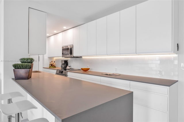 3 Island Ave Unit 12E, Miami Beach, FL 33139 - kitchen with tasteful backsplash, appliances with stainless steel finishes, a breakfast bar area, white cabinetry, and recessed lighting