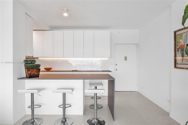 3 Island Ave Unit 12E, Miami Beach, FL 33139 - kitchen with a breakfast bar area, backsplash, white cabinetry, a peninsula, and modern cabinets