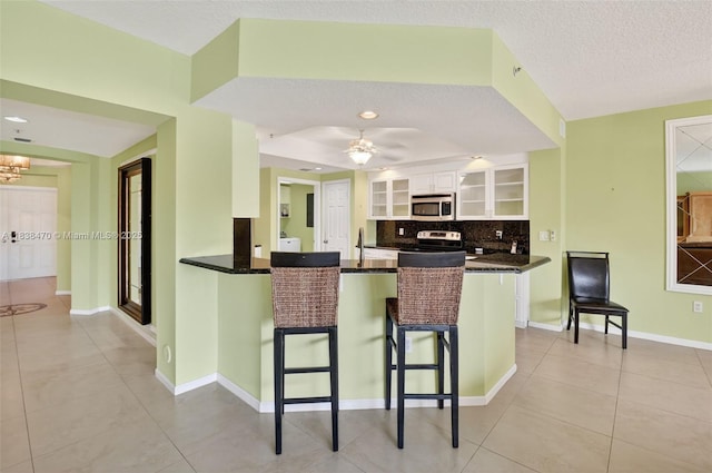5938 Crystal Shores Dr Unit 103, Boynton Beach, FL 33437 - kitchen featuring stainless steel microwave, a kitchen bar, white cabinetry, a peninsula, and glass insert cabinets