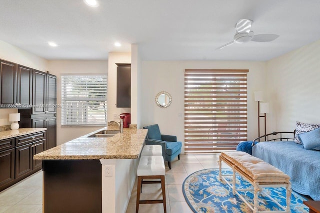 2851 W Prospect Rd Unit 1306, Tamarac, FL 33309 - kitchen featuring a breakfast bar area, light tile patterned floors, a ceiling fan, dark brown cabinetry, and light stone countertops