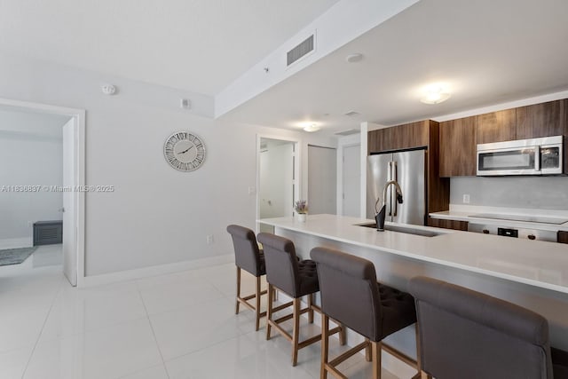 488 NE 18th St Unit 509, Miami, FL 33132 - kitchen with a breakfast bar area, stainless steel appliances, brown cabinetry, modern cabinets, and light countertops