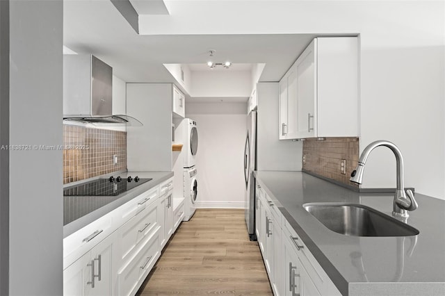 5077 NW 7th St Unit Ph15, Miami, FL 33126 - kitchen with wall chimney range hood, stacked washer / dryer, black electric cooktop, freestanding refrigerator, and white cabinets