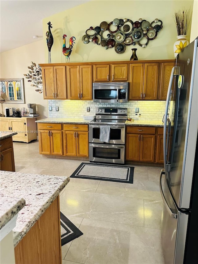 kitchen featuring appliances with stainless steel finishes, brown cabinets, tasteful backsplash, and light stone countertops
