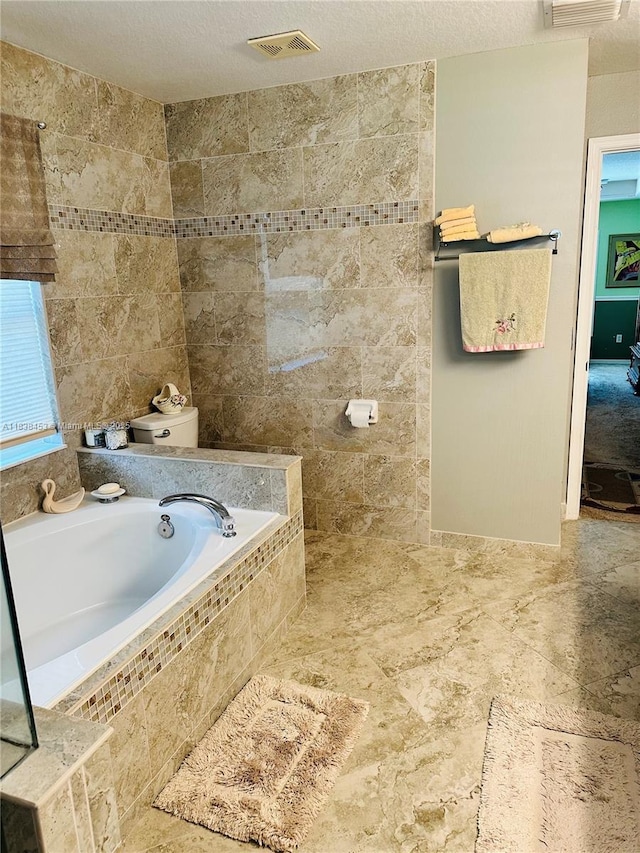 bathroom featuring a garden tub, tile walls, and a textured ceiling