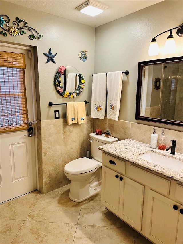 bathroom with tile walls, vanity, tile patterned flooring, and a wainscoted wall