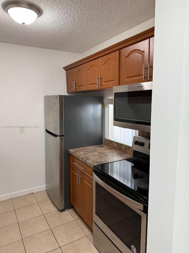 8560 N Sherman Cir Unit 105, Miramar, FL 33025 - kitchen with appliances with stainless steel finishes, dark countertops, a textured ceiling, light tile patterned floors, and brown cabinets
