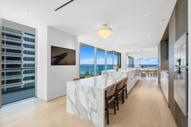 10203 Collins Ave Unit 701, Bal Harbour, FL 33154 - kitchen with modern cabinets, light wood-type flooring, a large island with sink, light stone counters, and a wall of windows