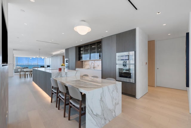 10203 Collins Ave Unit 701, Bal Harbour, FL 33154 - kitchen with modern cabinets, stainless steel oven, a kitchen bar, glass insert cabinets, and light wood-style flooring