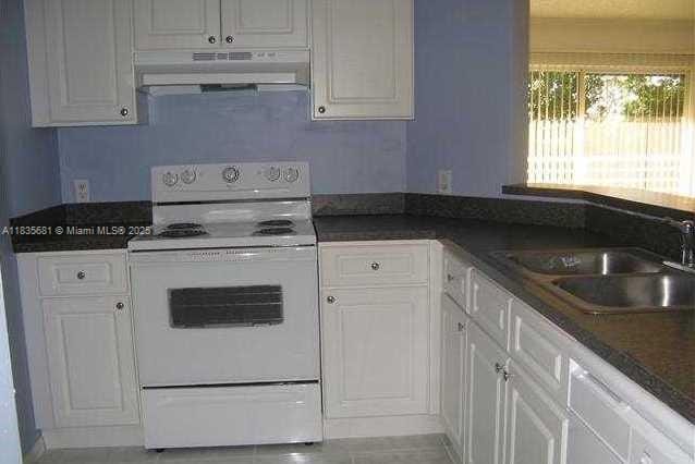 3421 NW 44th St Unit 103, Oakland Park, FL 33309 - kitchen featuring white electric range, under cabinet range hood, white cabinets, dark countertops, and light tile patterned flooring