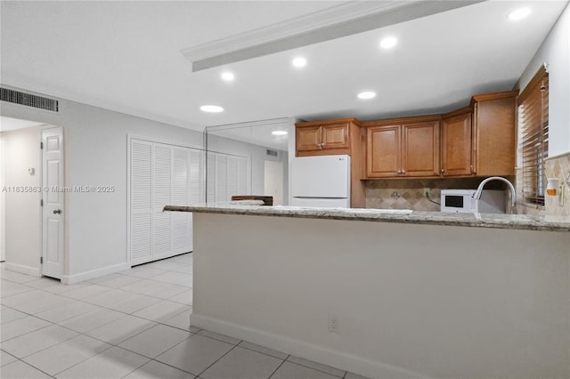 2400 NE 10th St Unit 104, Pompano Beach, FL 33062 - kitchen with freestanding refrigerator, tasteful backsplash, recessed lighting, brown cabinets, and light stone counters