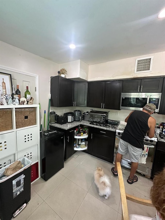 1249 S Flamingo Rd, Davie, FL 33325 - kitchen featuring stainless steel microwave, dark cabinetry, range, light tile patterned floors, and fridge
