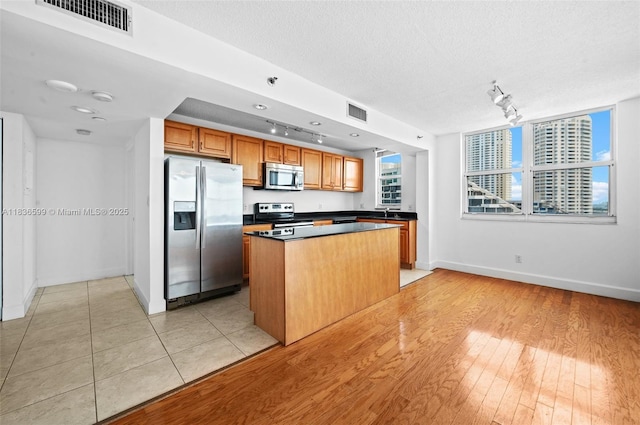770 Claughton Island Dr Unit 1915, Miami, FL 33131 - kitchen featuring appliances with stainless steel finishes, rail lighting, a center island, brown cabinetry, and dark countertops