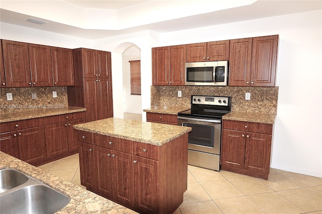 3001 SW 156th Ave, Miami, FL 33185 - kitchen featuring stainless steel appliances, light tile patterned flooring, decorative backsplash, arched walkways, and a kitchen island
