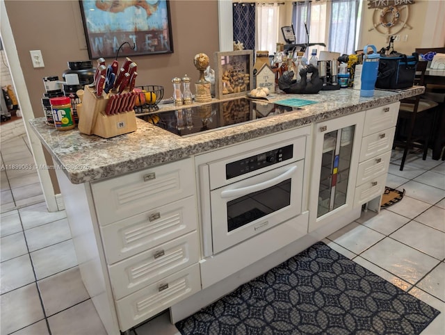 2606 Gulfstream Ln, Fort Lauderdale, FL 33312 - kitchen with black electric stovetop, oven, light tile patterned flooring, and white cabinets