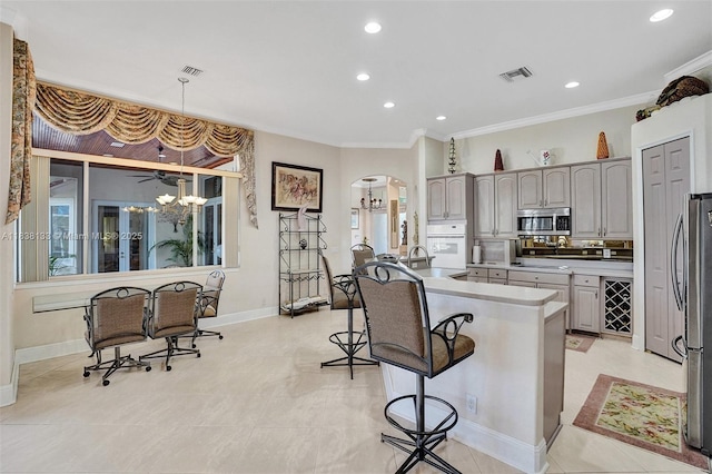 15595 Chandelle Pl, Wellington, FL 33414 - kitchen featuring appliances with stainless steel finishes, arched walkways, a kitchen bar, crown molding, and a center island with sink