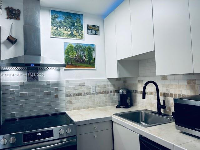2899 Collins Ave Unit 1504, Miami Beach, FL 33140 - kitchen with wall chimney exhaust hood, stainless steel appliances, white cabinets, and decorative backsplash
