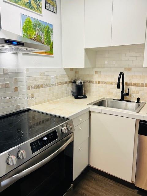 2899 Collins Ave Unit 1504, Miami Beach, FL 33140 - kitchen featuring stainless steel appliances, white cabinets, wall chimney range hood, and light countertops