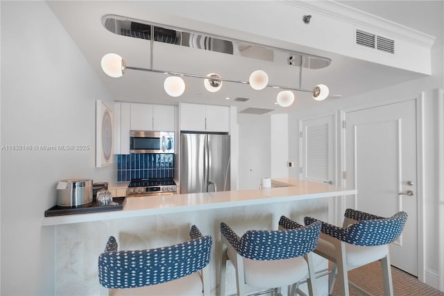 4401 Collins Ave Unit 2305, Miami Beach, FL 33140 - kitchen featuring stainless steel appliances, a breakfast bar, white cabinets, decorative backsplash, and a peninsula