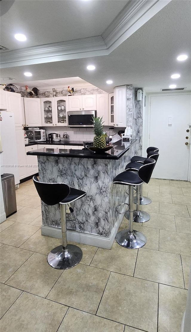 2750 NE 183rd St Unit 1701, Aventura, FL 33160 - kitchen featuring crown molding, stainless steel microwave, a kitchen breakfast bar, dark countertops, and white cabinets
