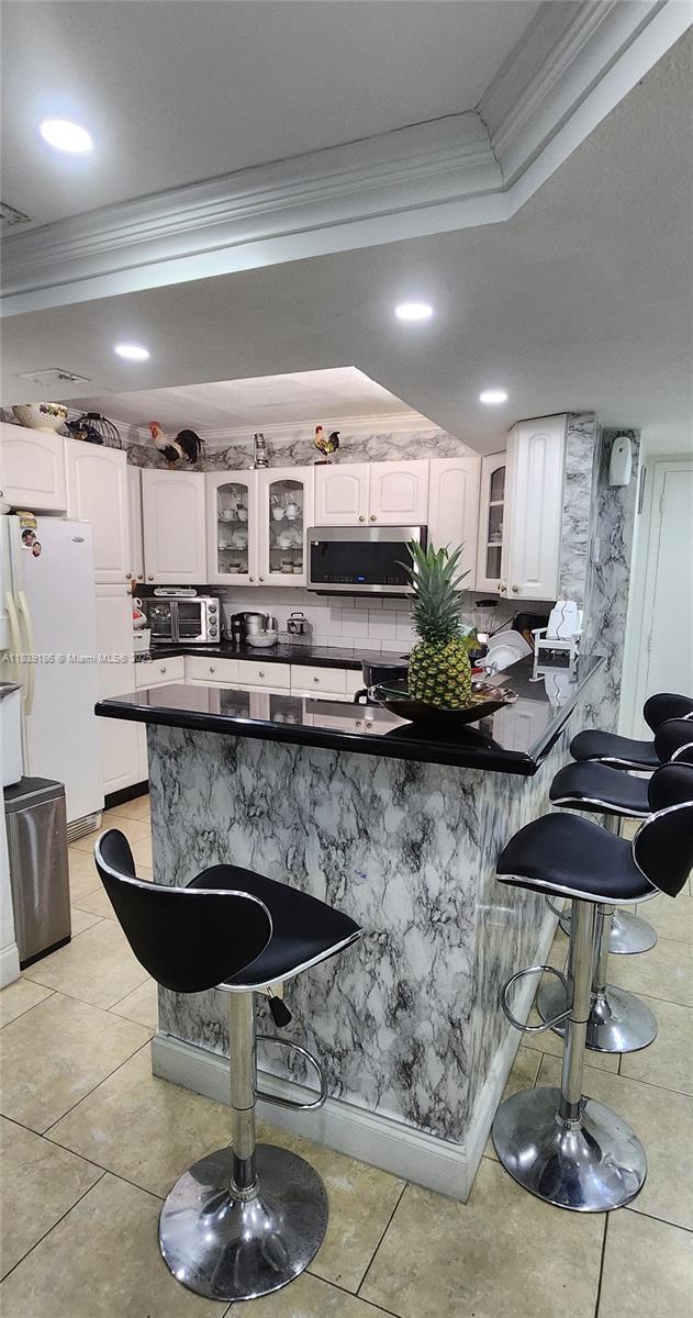 2750 NE 183rd St Unit 1701, Aventura, FL 33160 - kitchen featuring crown molding, a breakfast bar, a peninsula, stainless steel microwave, and dark countertops