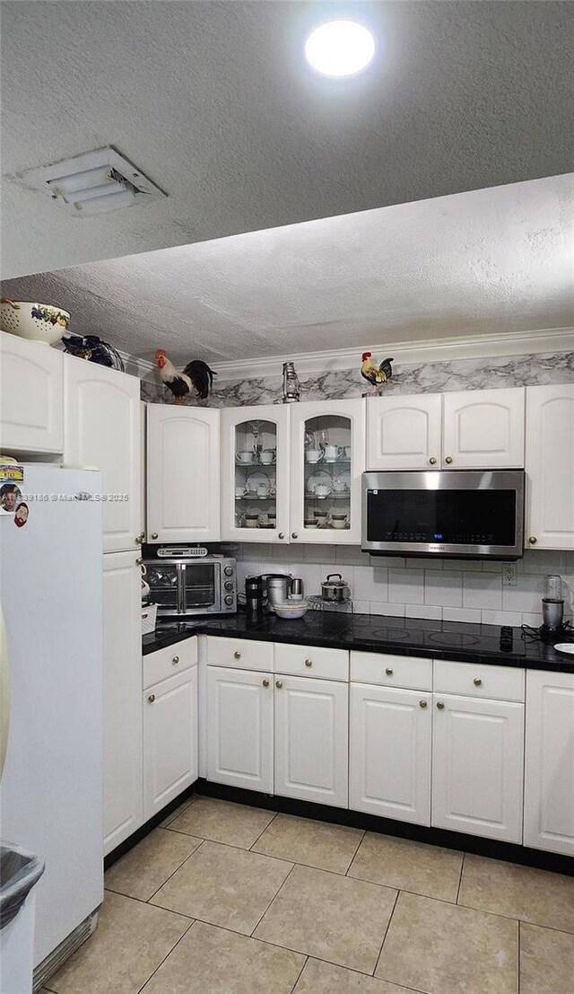 2750 NE 183rd St Unit 1701, Aventura, FL 33160 - kitchen featuring stainless steel microwave, freestanding refrigerator, dark countertops, white cabinets, and light tile patterned floors