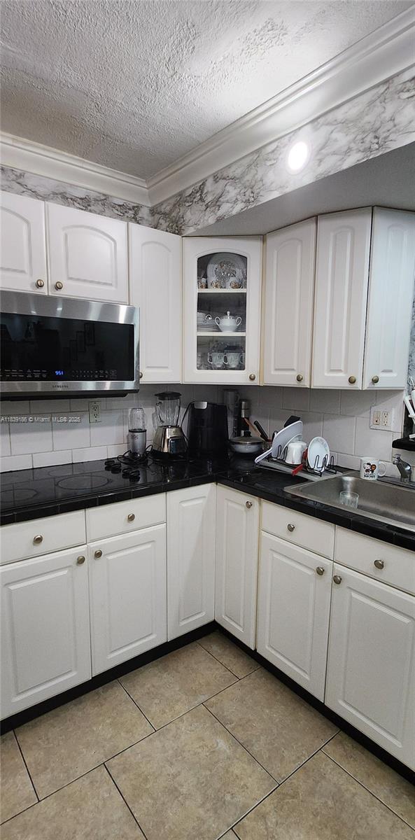 2750 NE 183rd St Unit 1701, Aventura, FL 33160 - kitchen featuring stainless steel microwave, a textured ceiling, ornamental molding, dark countertops, and decorative backsplash