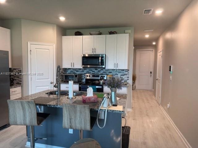 6349 Topsail Dr, West Palm Beach, FL 33413 - kitchen with stainless steel appliances, backsplash, light wood-type flooring, white cabinetry, and dark stone counters