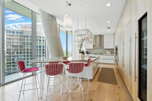 2675 S Bayshore Dr Unit 1601S, Miami, FL 33133 - kitchen featuring modern cabinets, white cabinetry, light wood finished floors, decorative backsplash, and a kitchen bar