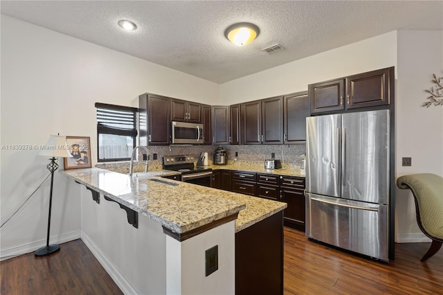 5506 Redhawk Dr, New Port Richey, FL 34655 - kitchen featuring appliances with stainless steel finishes, a peninsula, dark brown cabinetry, light stone countertops, and dark wood-style flooring