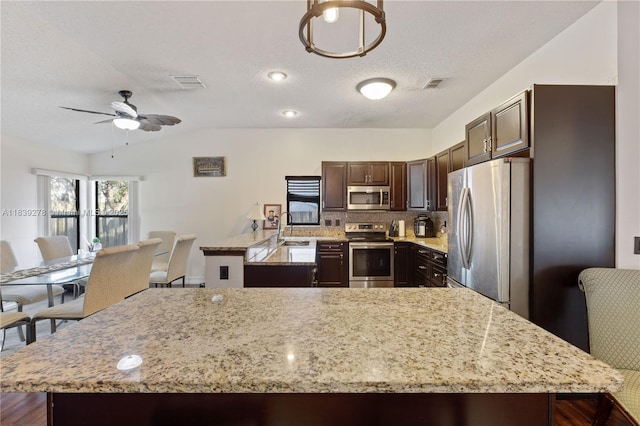 5506 Redhawk Dr, New Port Richey, FL 34655 - kitchen featuring stainless steel appliances, vaulted ceiling, light stone countertops, dark brown cabinets, and a ceiling fan