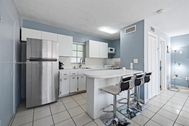 590 SW 62nd Ave, Miami, FL 33144 - kitchen featuring freestanding refrigerator, light countertops, white cabinetry, a kitchen bar, and a peninsula